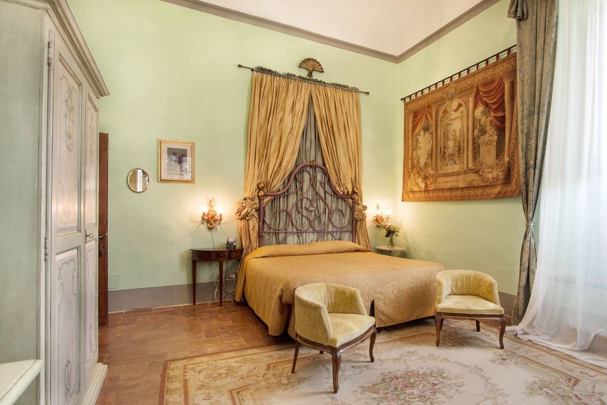 Une chambre à coucher avec un lit, deux chaises, une table de chevet, une horloge murale et un tableau.