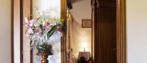 A hallway with a wooden floor, a vase of flowers, and a lamp.