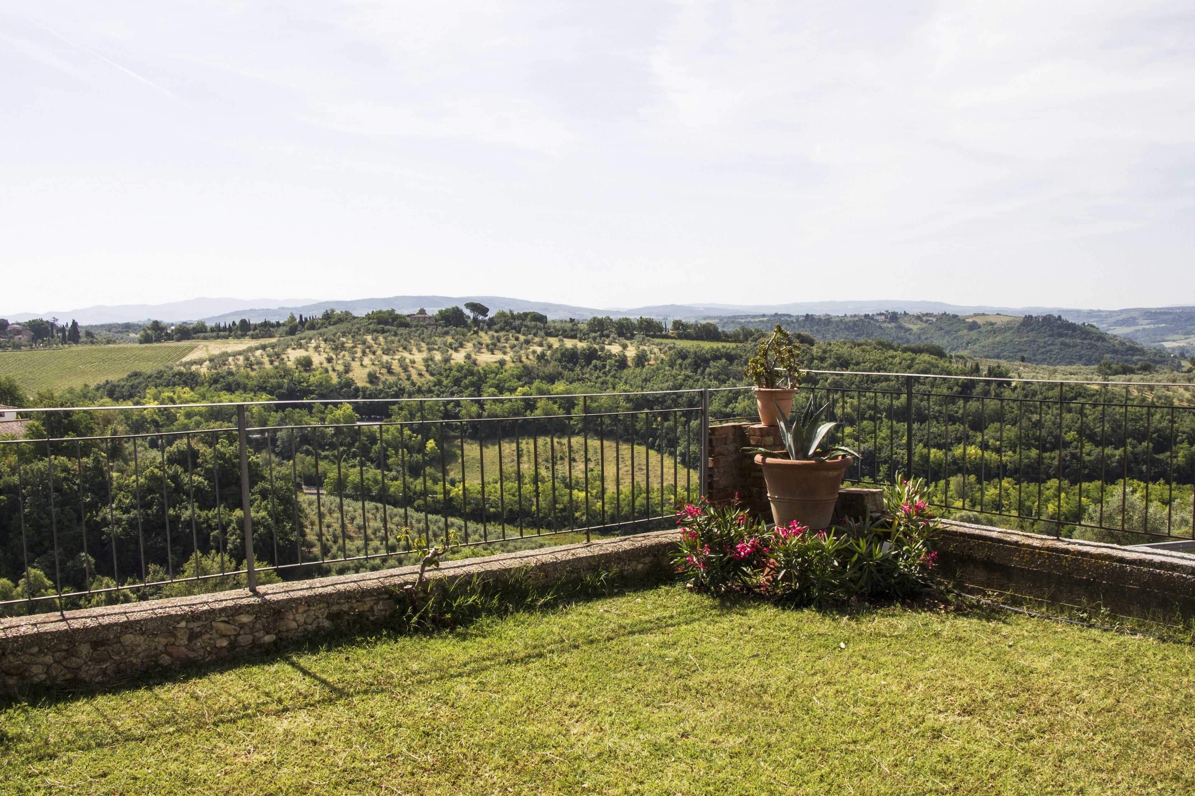 A terrace with a stone wall, potted plants, and a view of rolling hills and vineyards.