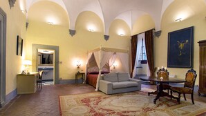 Ein Schlafzimmer mit einem Himmelbett, einer Couch, einem Esstisch mit Stühlen und einem großen Gemälde an der Wand.