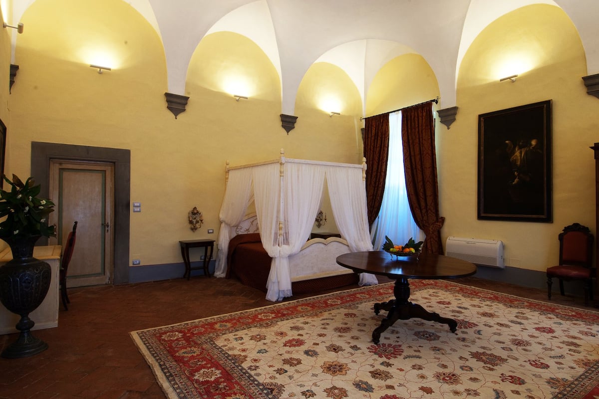 Une chambre avec un lit à baldaquin, une table ronde et un grand tableau accroché au mur.