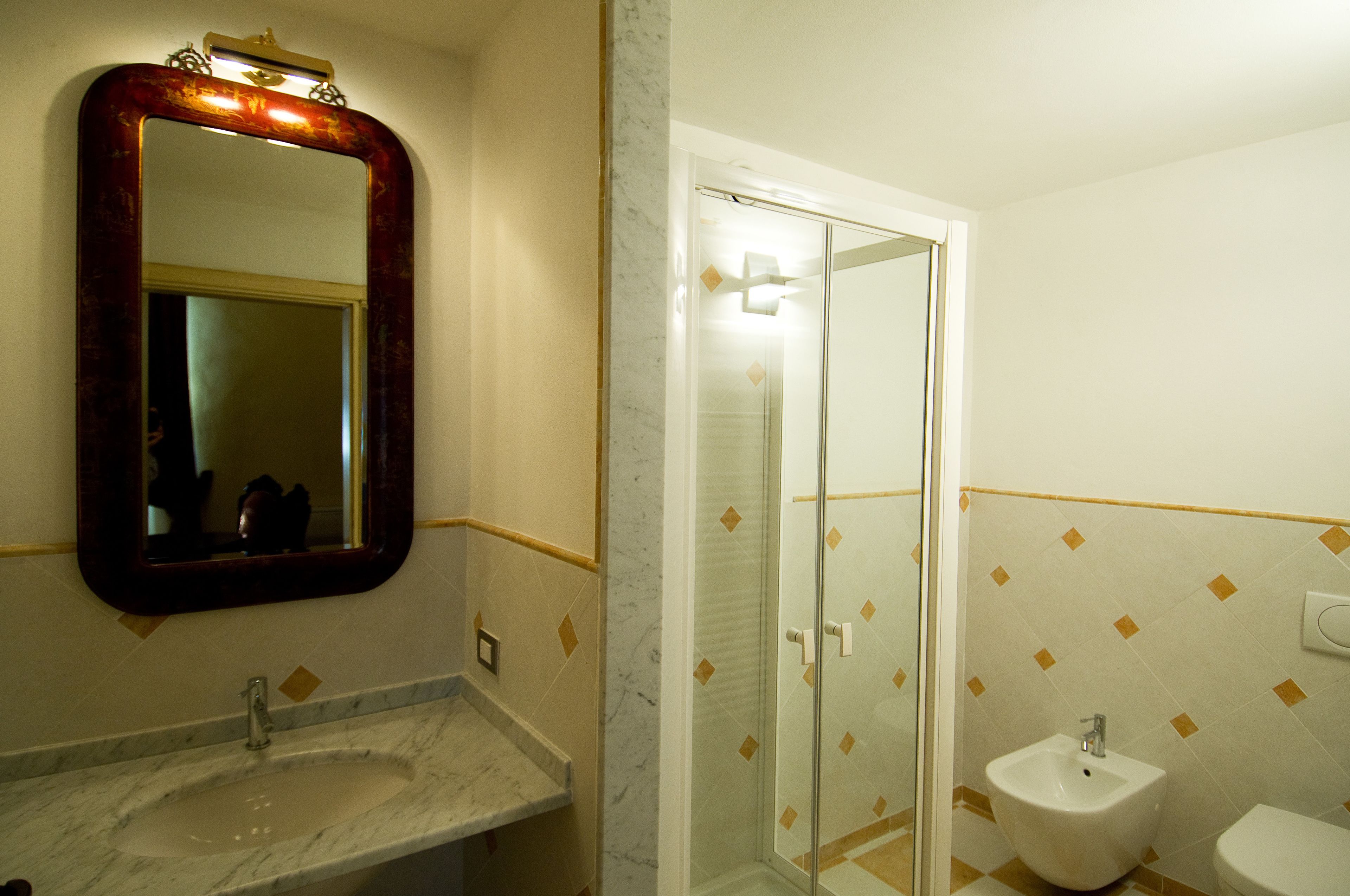 A bathroom with a marble sink, a large mirror, a glass shower enclosure, and a white pedestal sink.