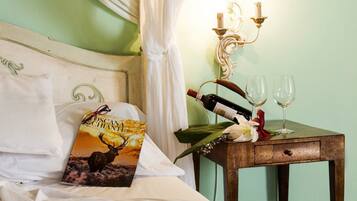 A bed with a book titled "Scena e Chianti" and a pair of glasses, a wooden nightstand with a wine bottle and two glasses, and a wall-mounted light fixture.