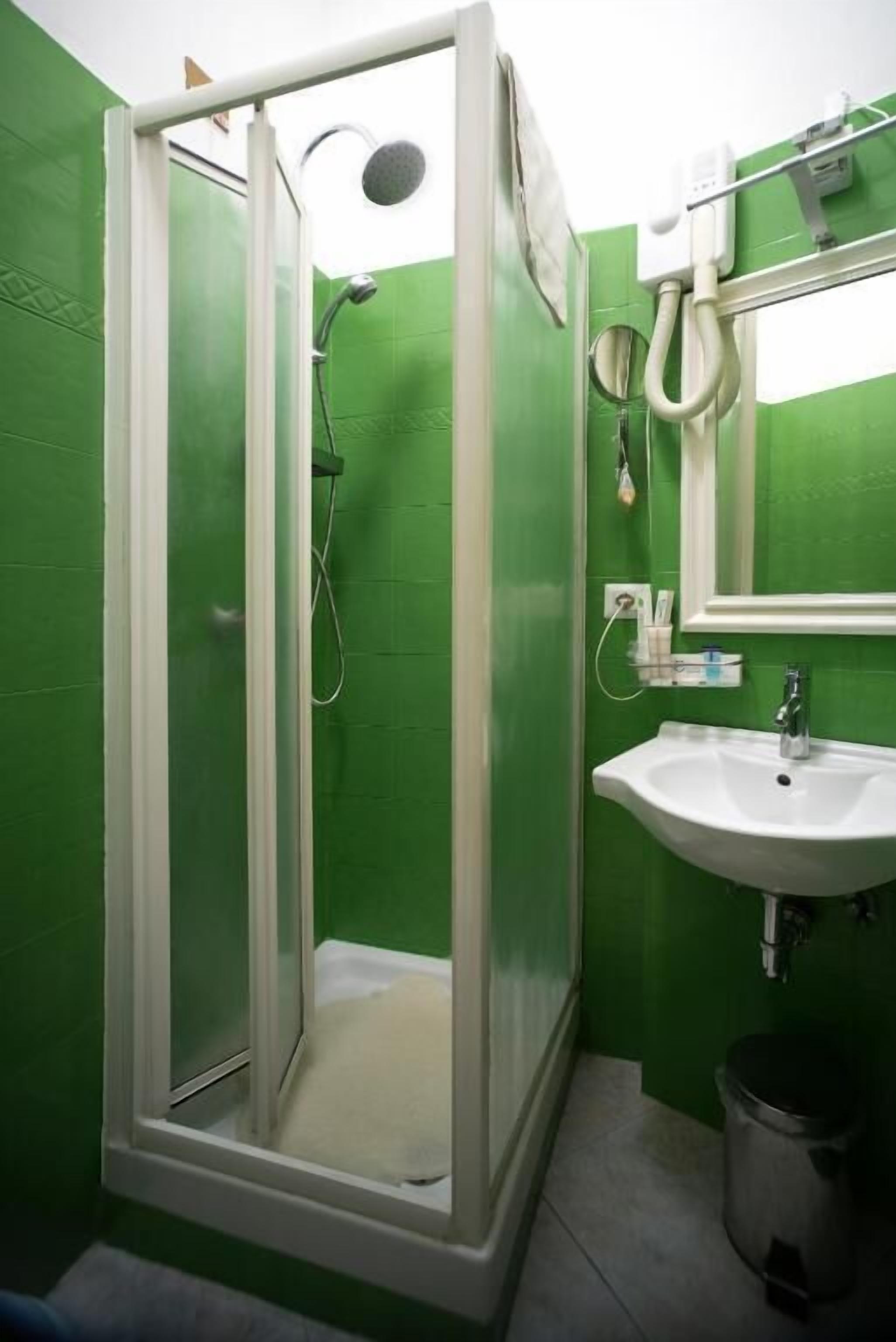 A bathroom with a green tiled wall, a white sink, and a glass-enclosed shower.
