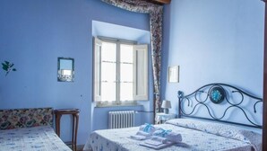 Quarto com duas camas, uma janela, um radiador e uma mesinha.