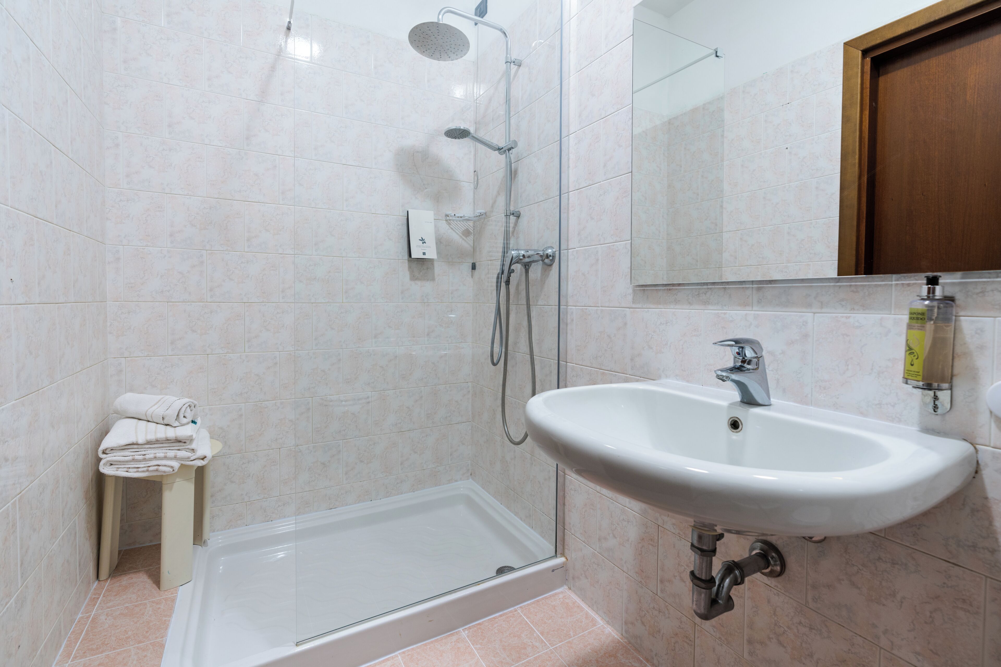 Un baño con ducha, lavamanos y un taburete pequeño con toallas.