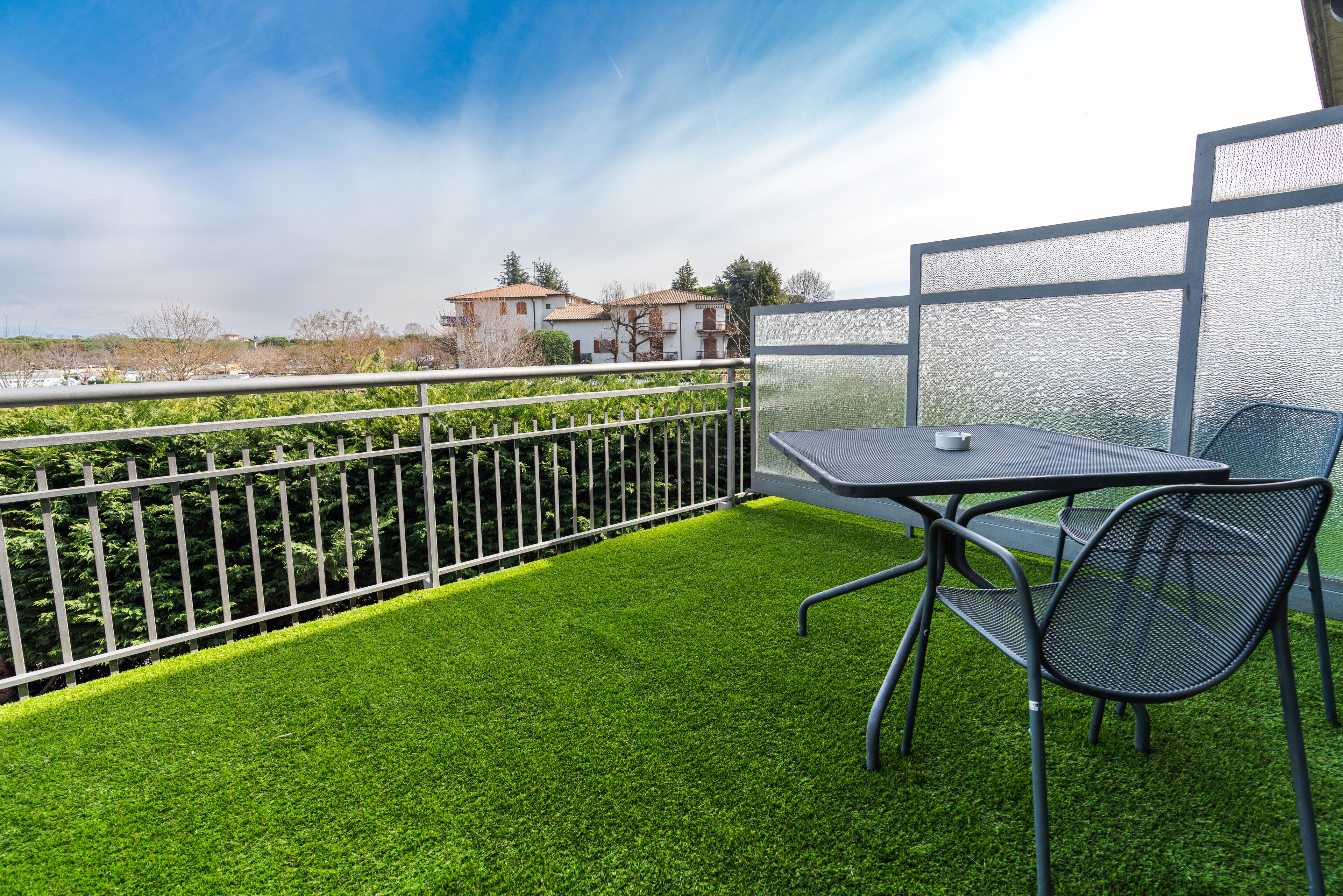 Ein Balkon mit künstlichem Rasen, einem Metalltisch und zwei Stühlen.