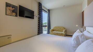 Quarto de hotel com uma cama, uma cadeira, uma televisão e uma janela com cortinas.