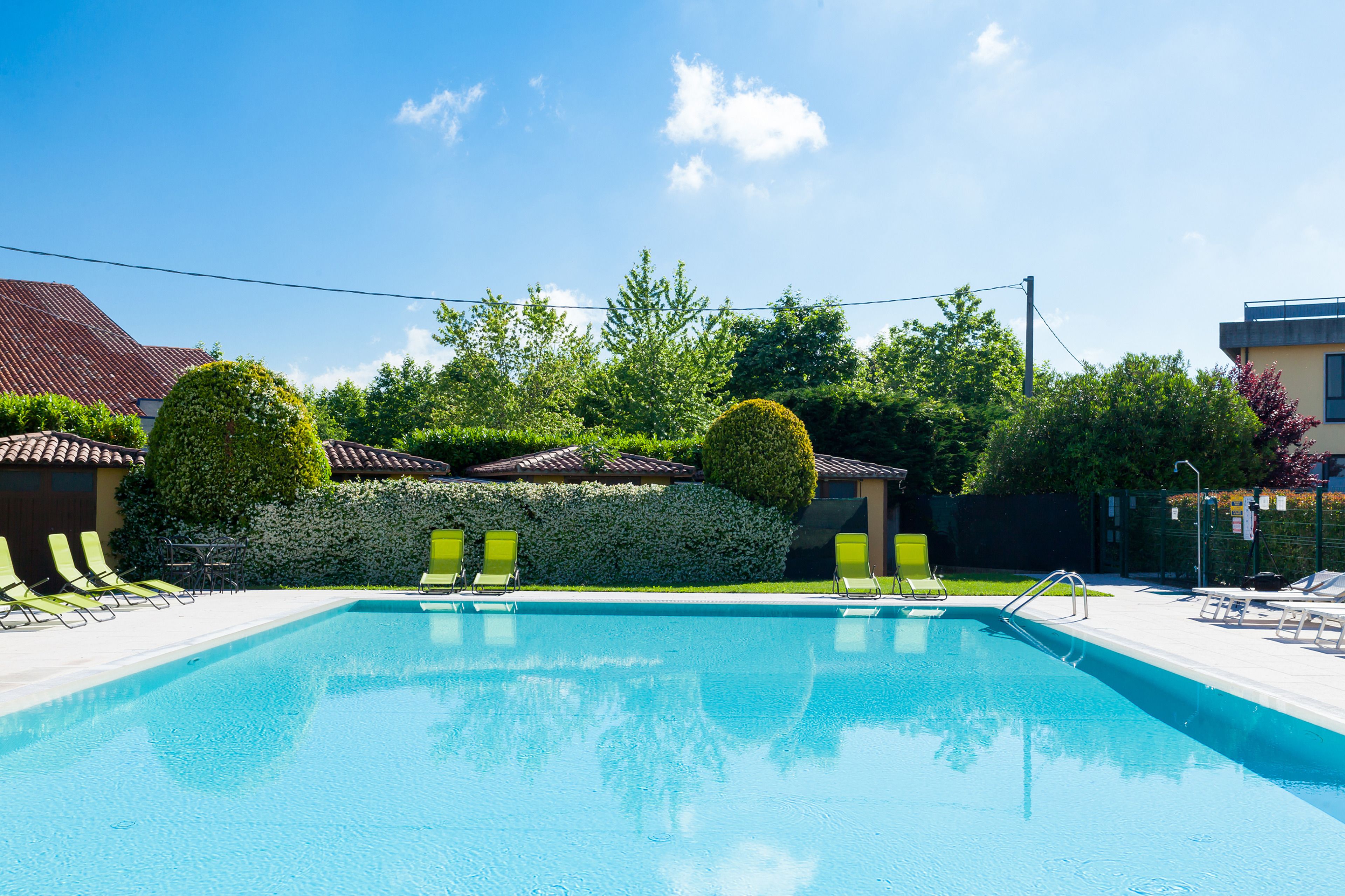 Una piscina con sillas de descanso verdes y un seto.