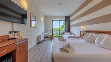 A hotel room with a bed, a desk, a flat-screen TV, a chair, a small table, and a window with curtains.