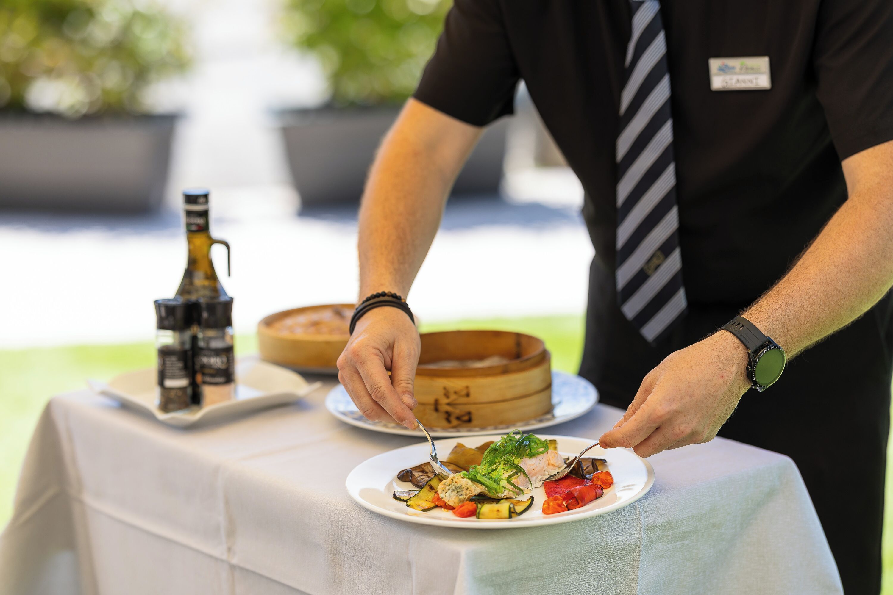 A person serving food on a table with a bottle and a wooden container in the background.
