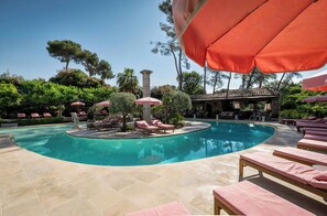 A pool area with lounge chairs and umbrellas, surrounded by trees and a stone building.
