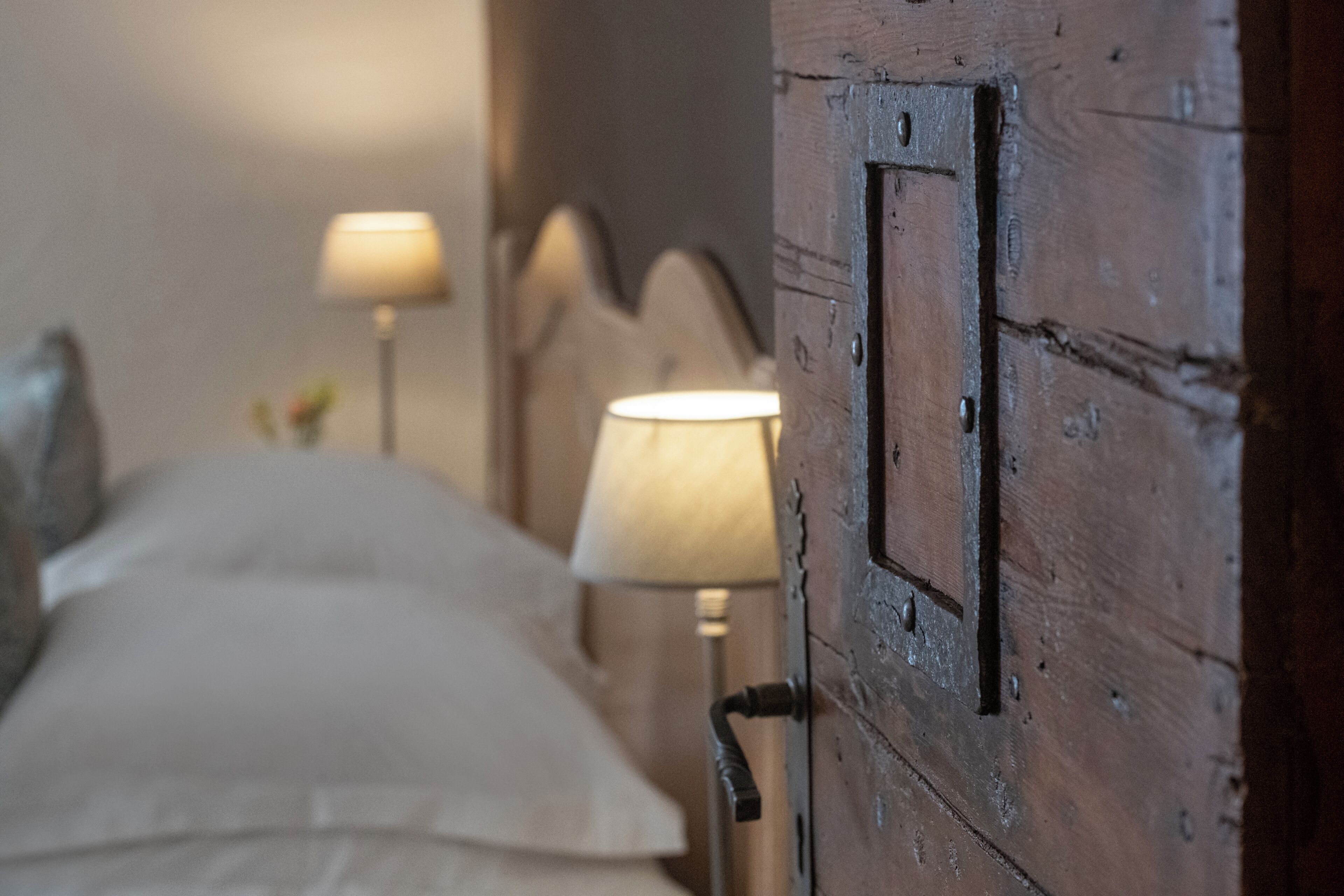 A wooden door with a metal handle, a bed with white linens, and a bedside lamp.