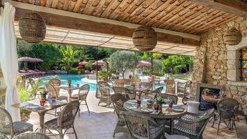 An outdoor patio with wicker furniture, a pool, and stone walls.