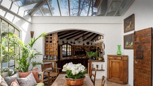 A sunlit room with a wooden table, chairs, a bench, and a potted plant. - Hotel Les Messugues (Saint-Paul-de-Vence)
