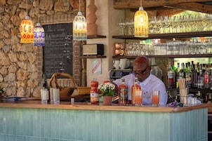 Zona de bar con pared de piedra, luces colgantes y un barman preparando bebidas.