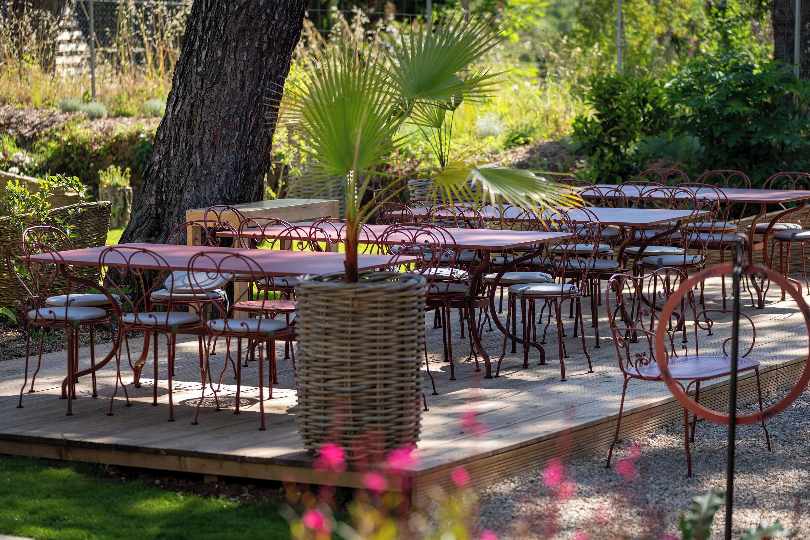 An outdoor dining area with wicker tables and chairs, surrounded by greenery and trees.