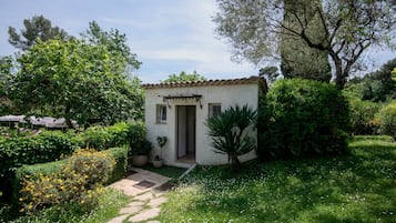 Un petit bâtiment d’un seul étage, doté d’un toit en tuiles, entouré d’une végétation luxuriante et accessible par un chemin de pierre menant à l’entrée.
