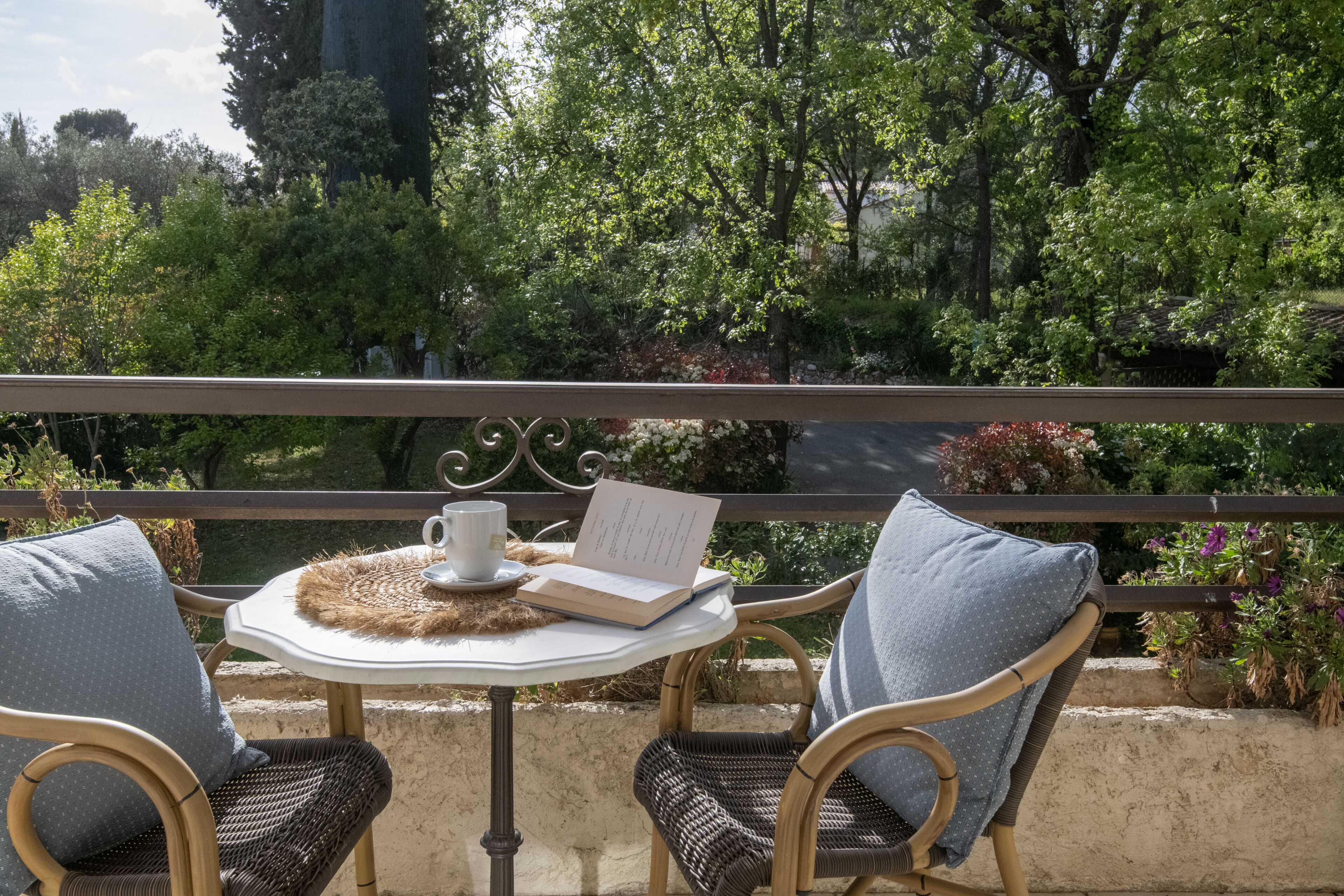 A balcony with wicker chairs, a table, a book, and a cup.