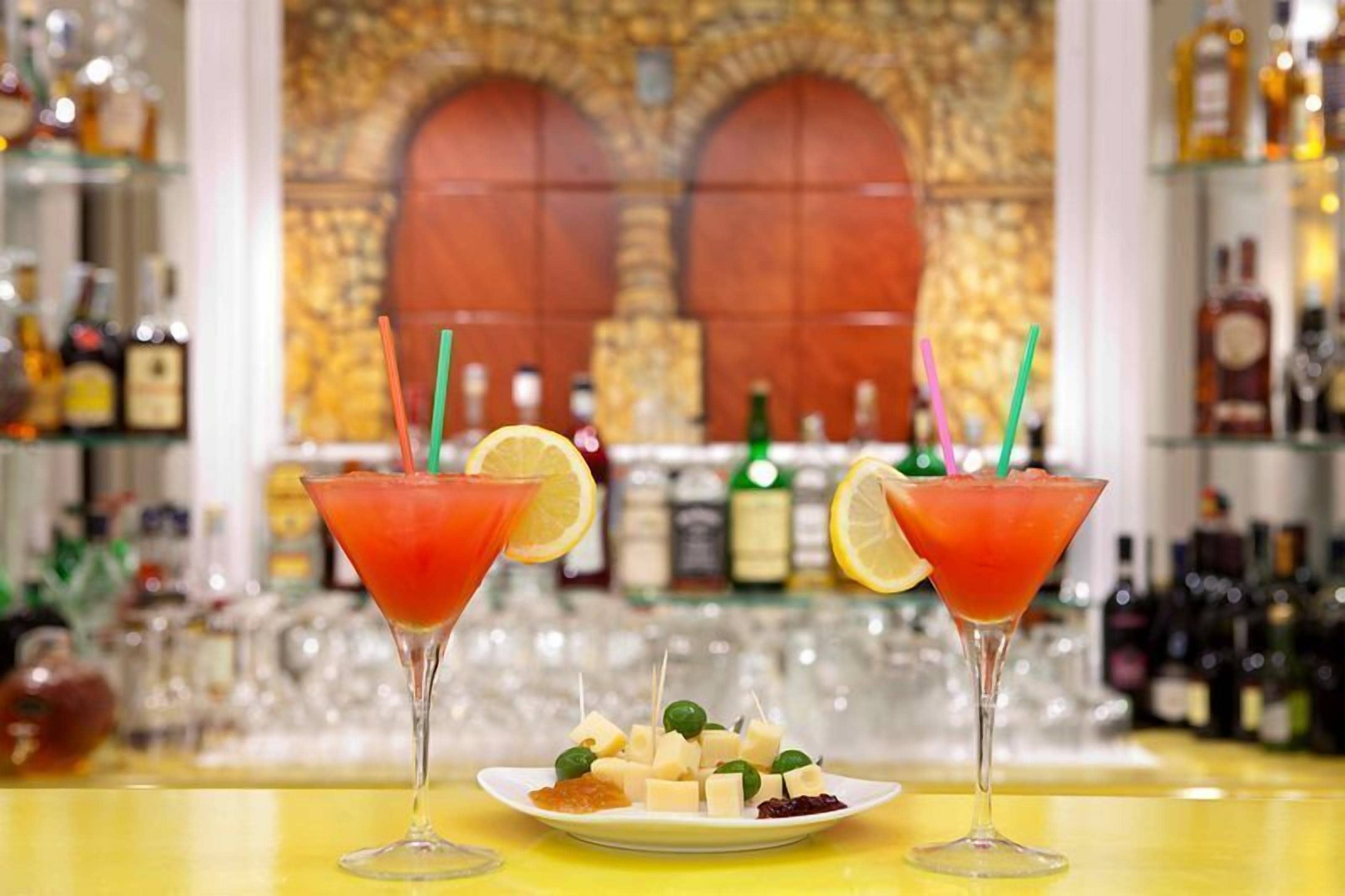 Two martini glasses with straws and lemon slices on a bar counter.