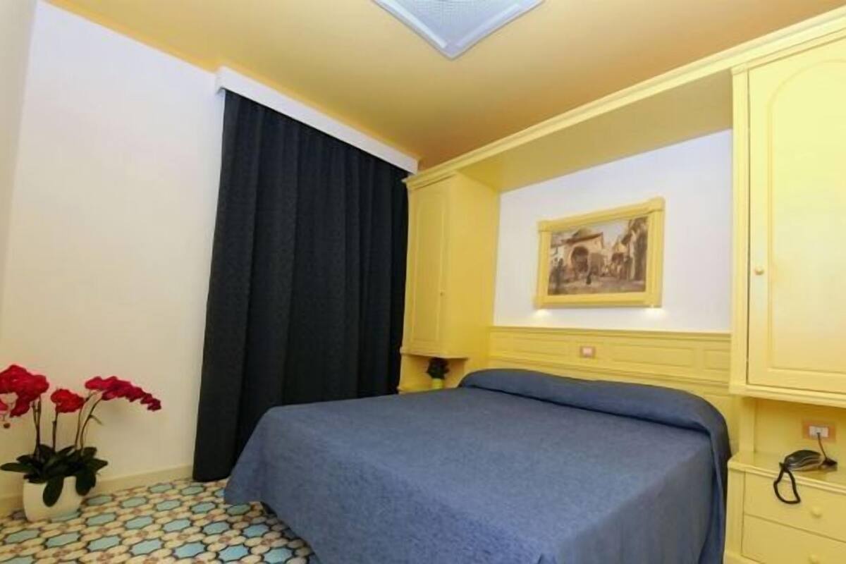 Una habitación de hotel con una cama, un cuadro en la pared, un teléfono y un florero con flores.