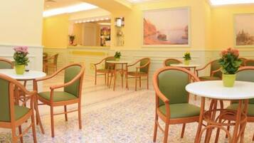 A hotel lobby with multiple round tables and green upholstered chairs, a patterned carpet, and artwork on the walls.
