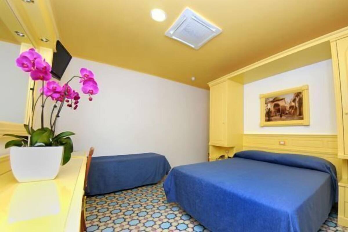 Una habitación con dos camas, un escritorio pequeño, una orquídea en maceta y un cuadro en la pared.