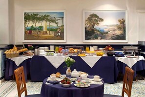 Un comedor con mesas dispuestas para el desayuno, que presenta una variedad de alimentos y un jarrón de flores.