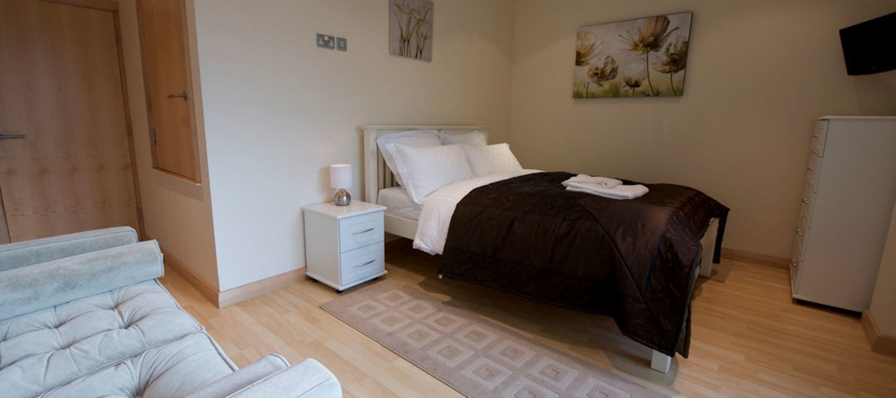 A bedroom with a bed, bedside table, lamp, and a small cabinet.