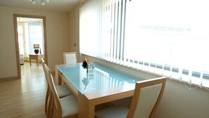 A spacious room with a wooden dining table, white chairs, a staircase, and a large window with blinds. - Dreamhouse Manchester Deansgate (Manchester)
