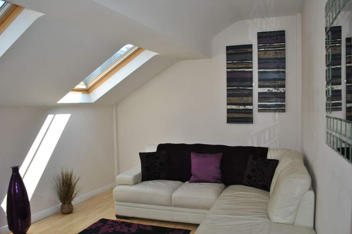 A modern living room with a white sofa, a large window, and a skylight.