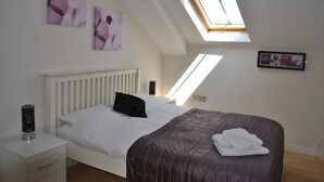 A bedroom with a sloped ceiling, skylight, white bed, dark brown bedspread, white bedside tables, and wall art. - Dreamhouse Manchester Deansgate (Manchester)