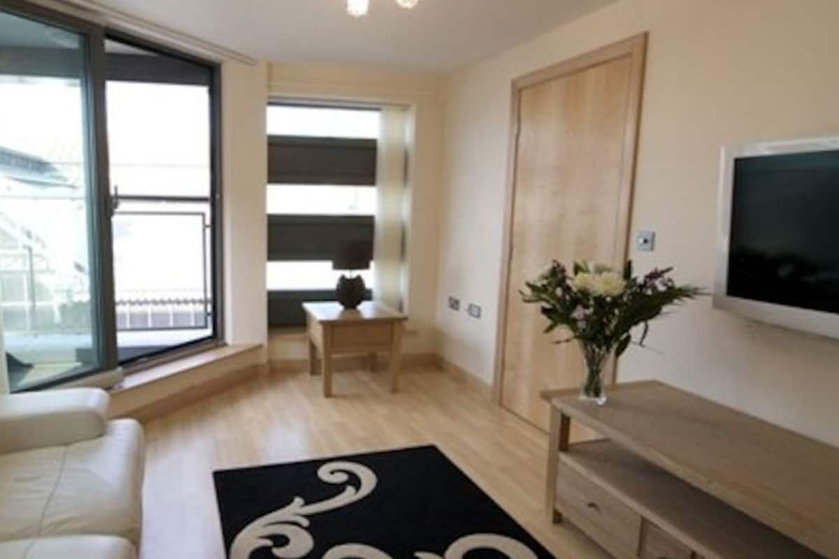 A modern living room with a sofa, a TV, a small table, and a window with blinds.