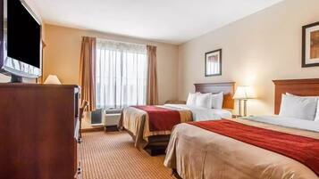 A hotel room with two beds, a television, a desk, and a window with curtains.