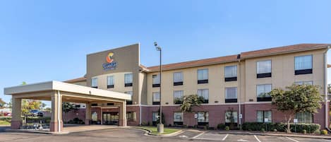 Un hotel con entrada cubierta, varios pisos y estacionamiento.
