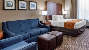 A hotel room with a large bed, a blue sofa, a wooden nightstand, and framed pictures on the wall. - Comfort Inn & Suites Atoka-Millington (Atoka)