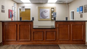 A reception desk with a wooden finish, a large wall clock, and a hand sanitizer dispenser. - Comfort Inn & Suites Atoka-Millington (Atoka)
