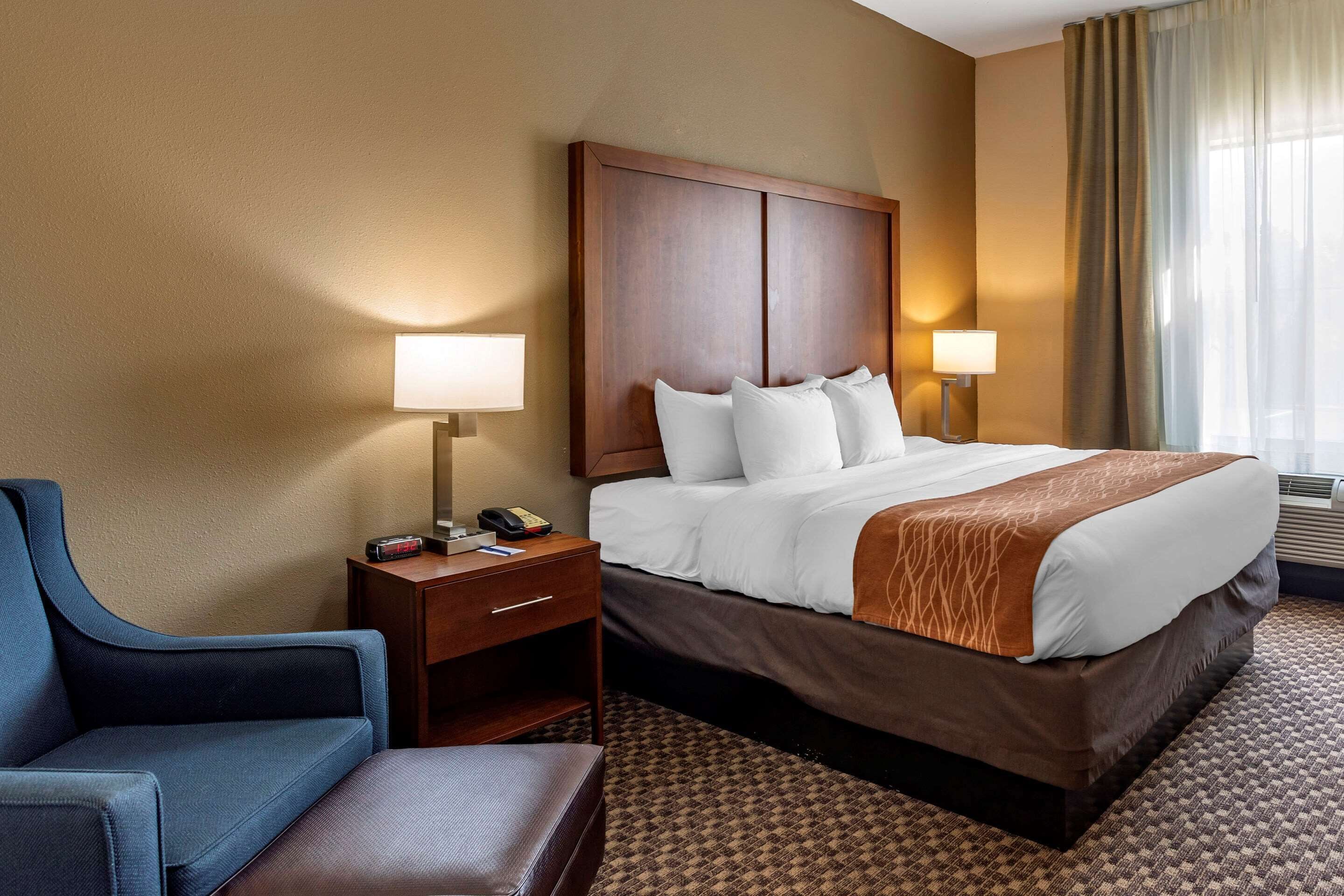 A hotel room with a large bed, two bedside tables with lamps, a blue armchair, and a patterned carpet.