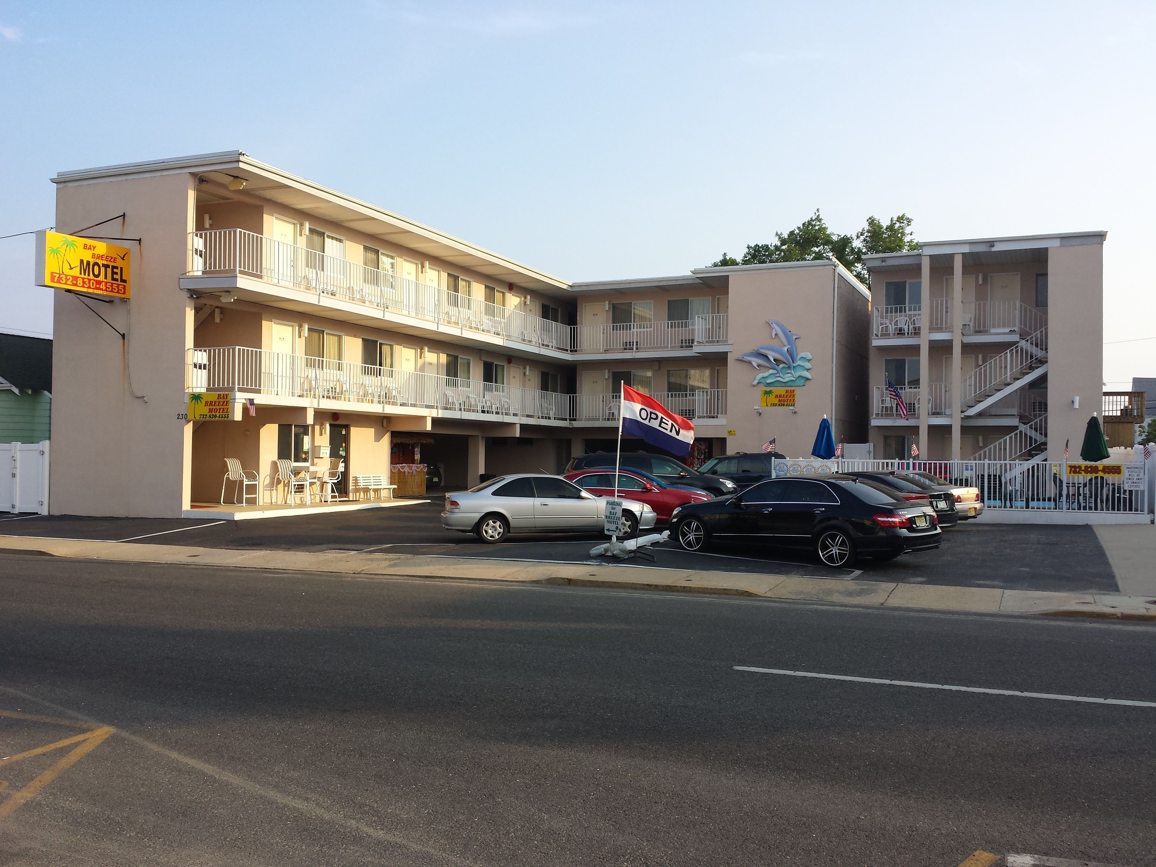 A motel with multiple balconies, a parking lot, and a flag indicating it's open.