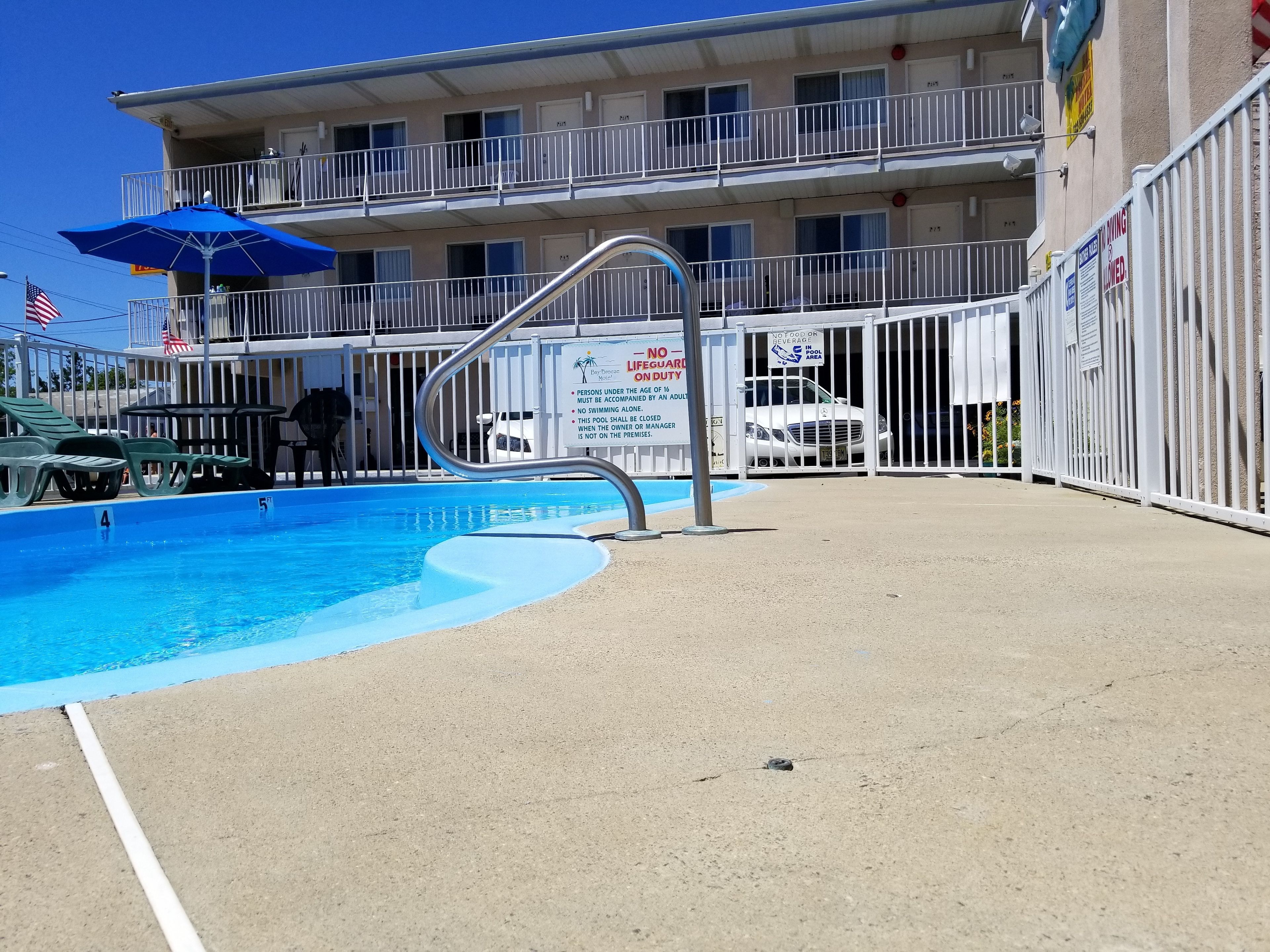 A swimming pool with a metal ladder, lounge chairs, and a blue umbrella.