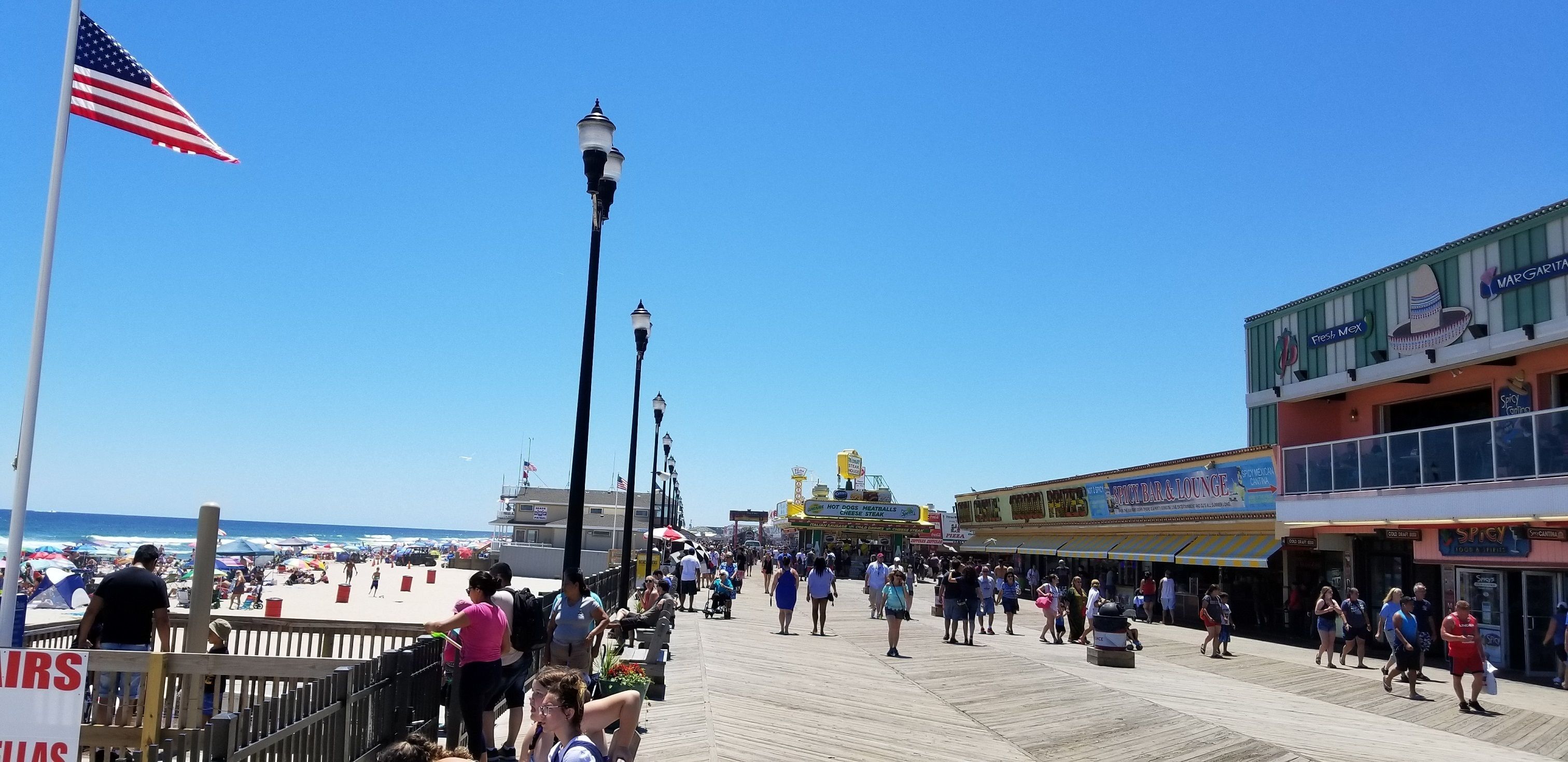 Un paseo marítimo con tiendas, una noria y una playa al fondo.