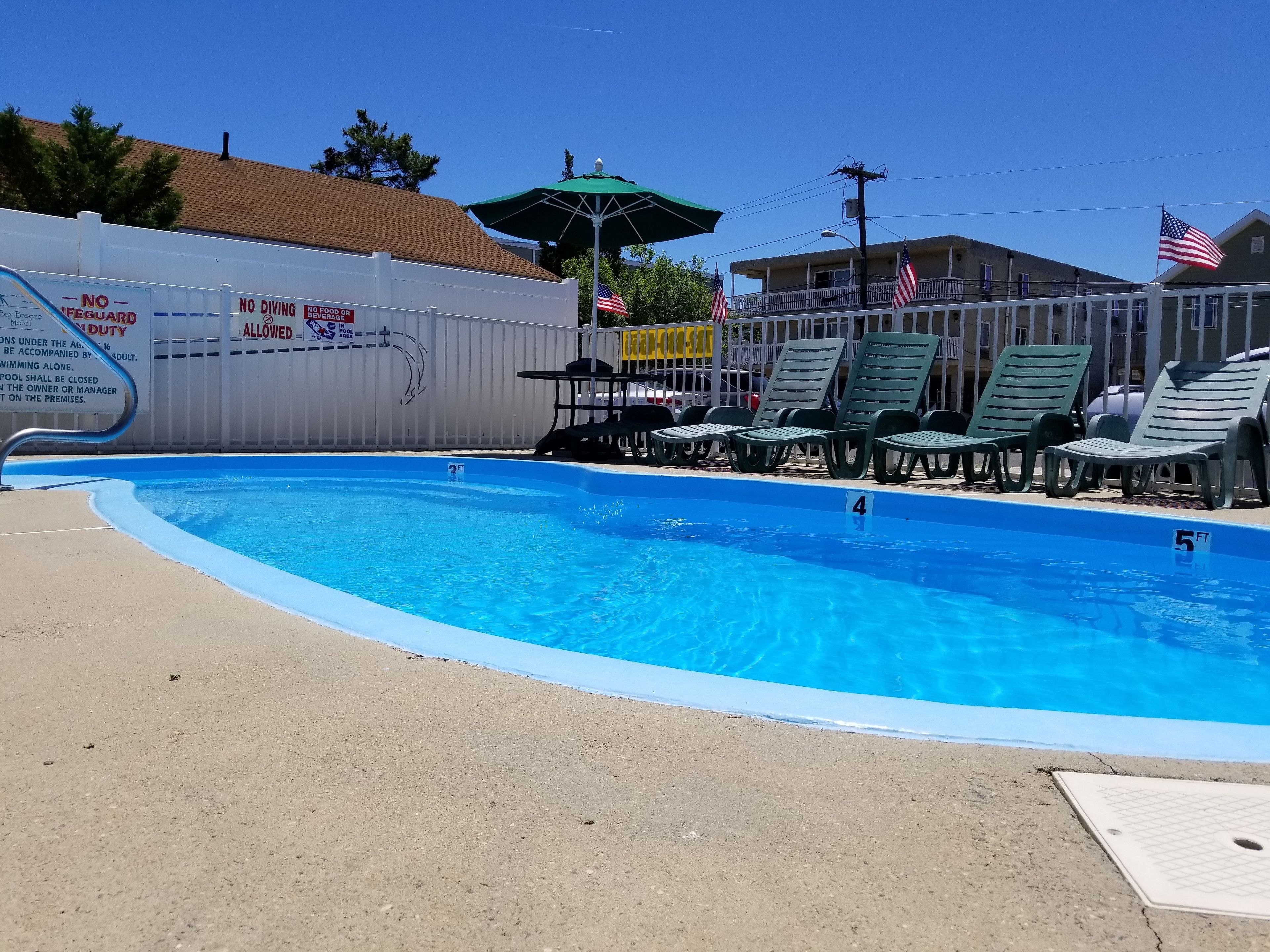 A swimming pool with lounge chairs, a lifeguard stand, and a fenced area with American flags.