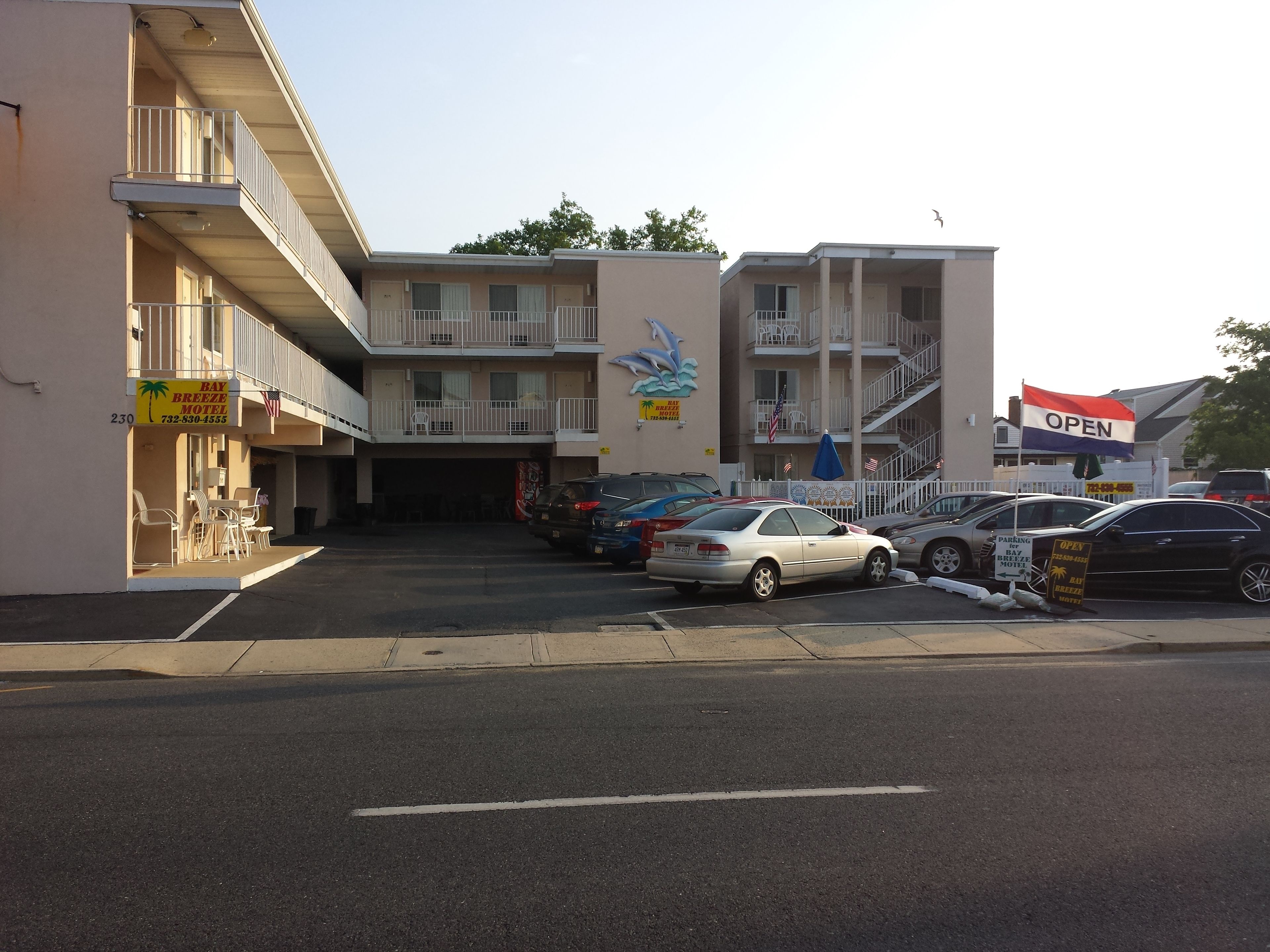 Un motel con estacionamiento, varios coches aparcados y un letrero que indica que está abierto.