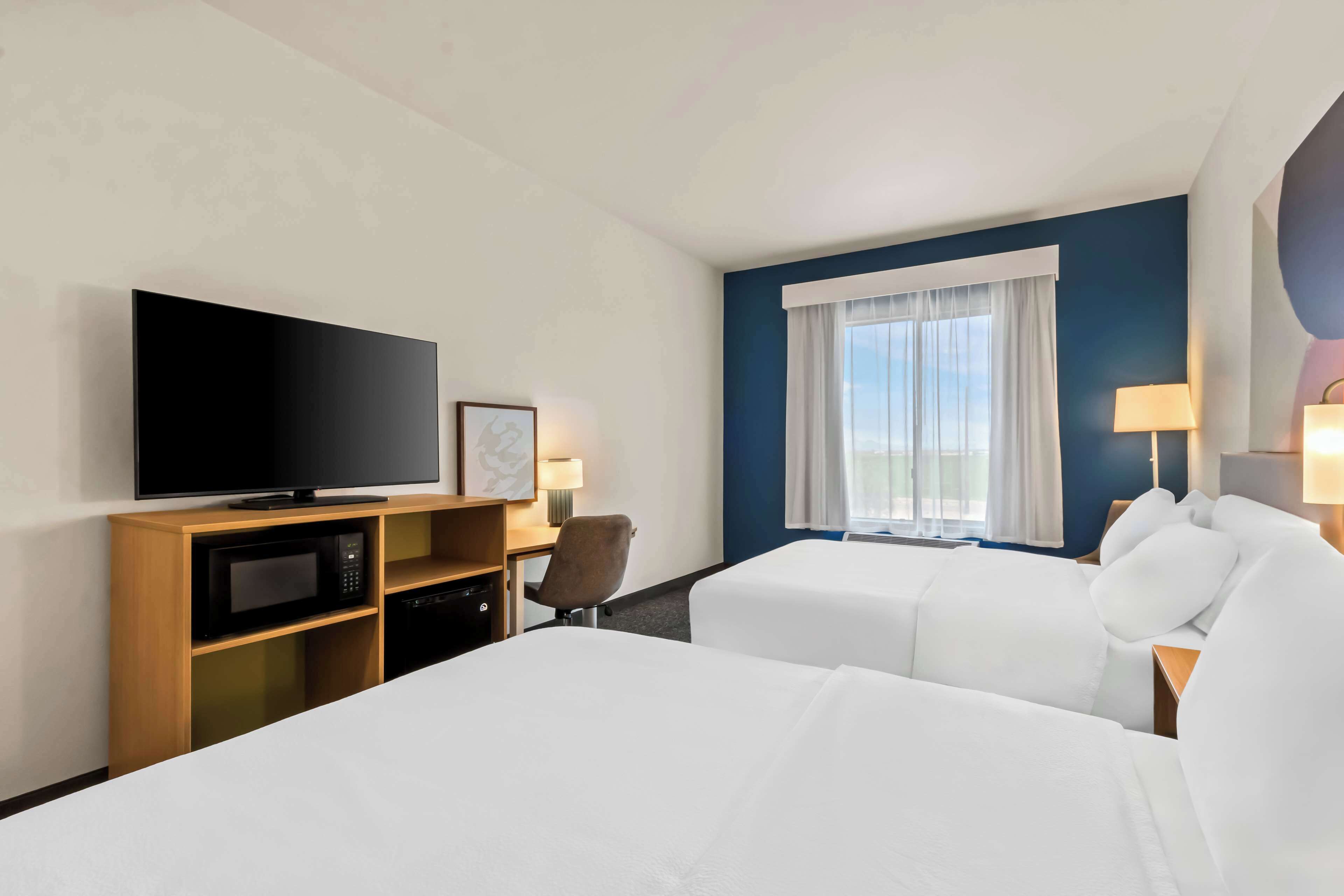 A hotel room with two beds, a television, a desk, and a window with curtains.