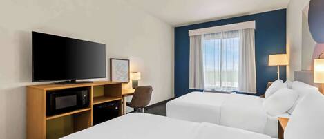 A hotel room with two beds, a television, a desk, and a window with curtains.