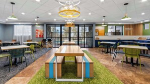 A modern dining area with a central wooden table, green and black chairs, and a green carpet.