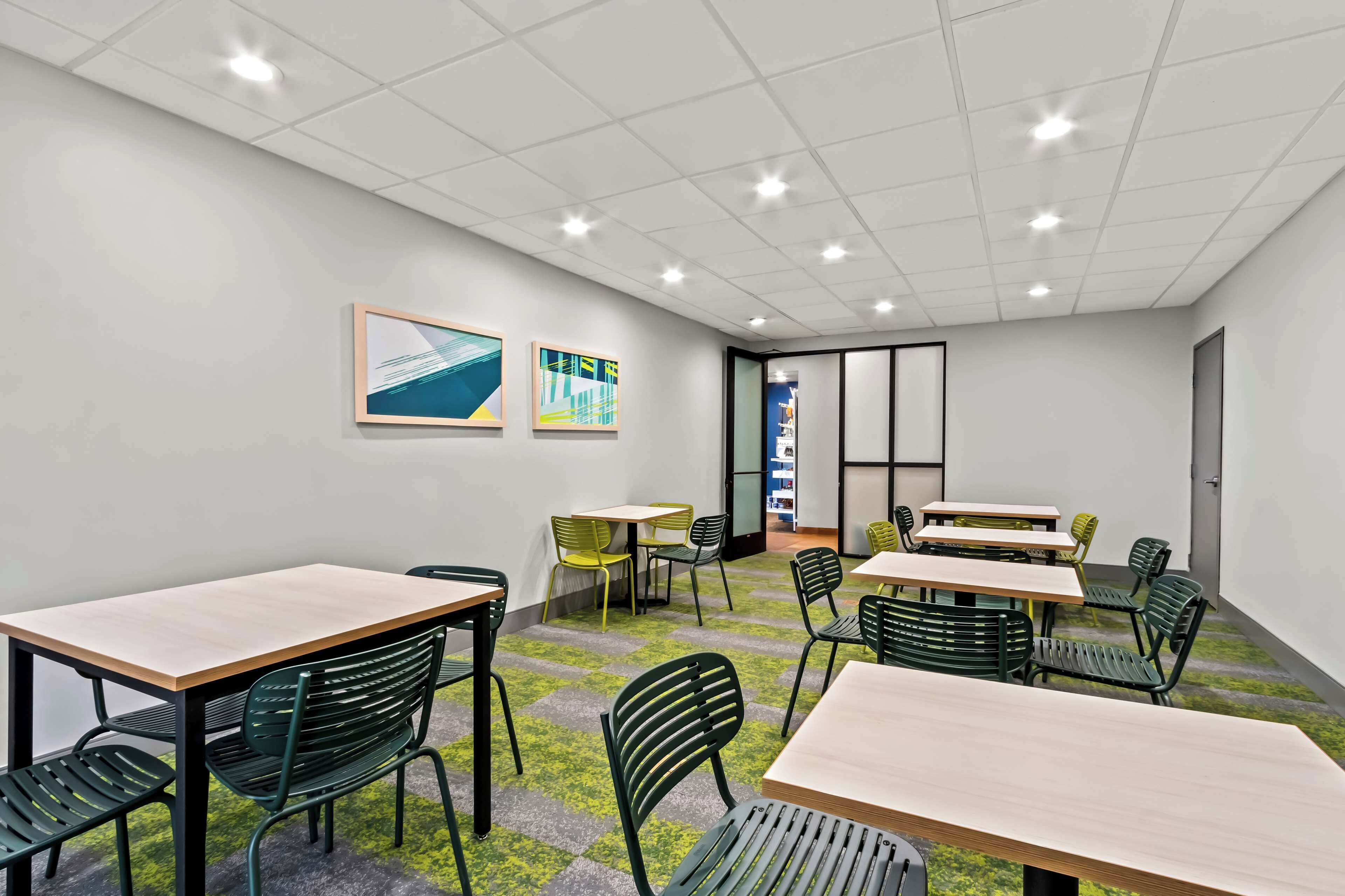 A modern meeting room with tables and chairs, a tiled ceiling, and artwork on the walls.