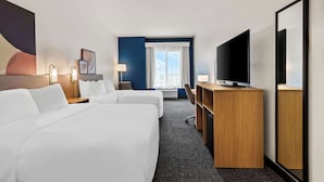 A hotel room with two beds, a desk, a television, and a large mirror.