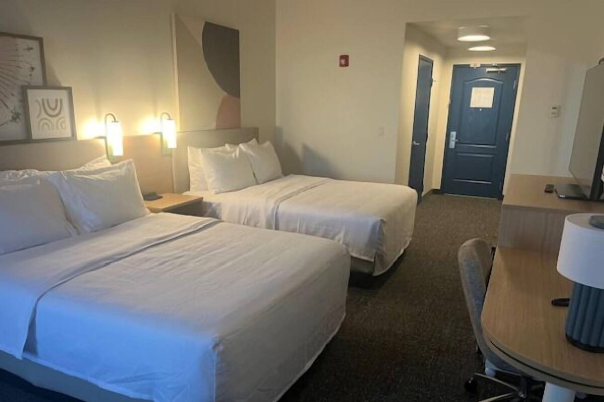 A hotel room with two beds, a desk, a chair, and a door.