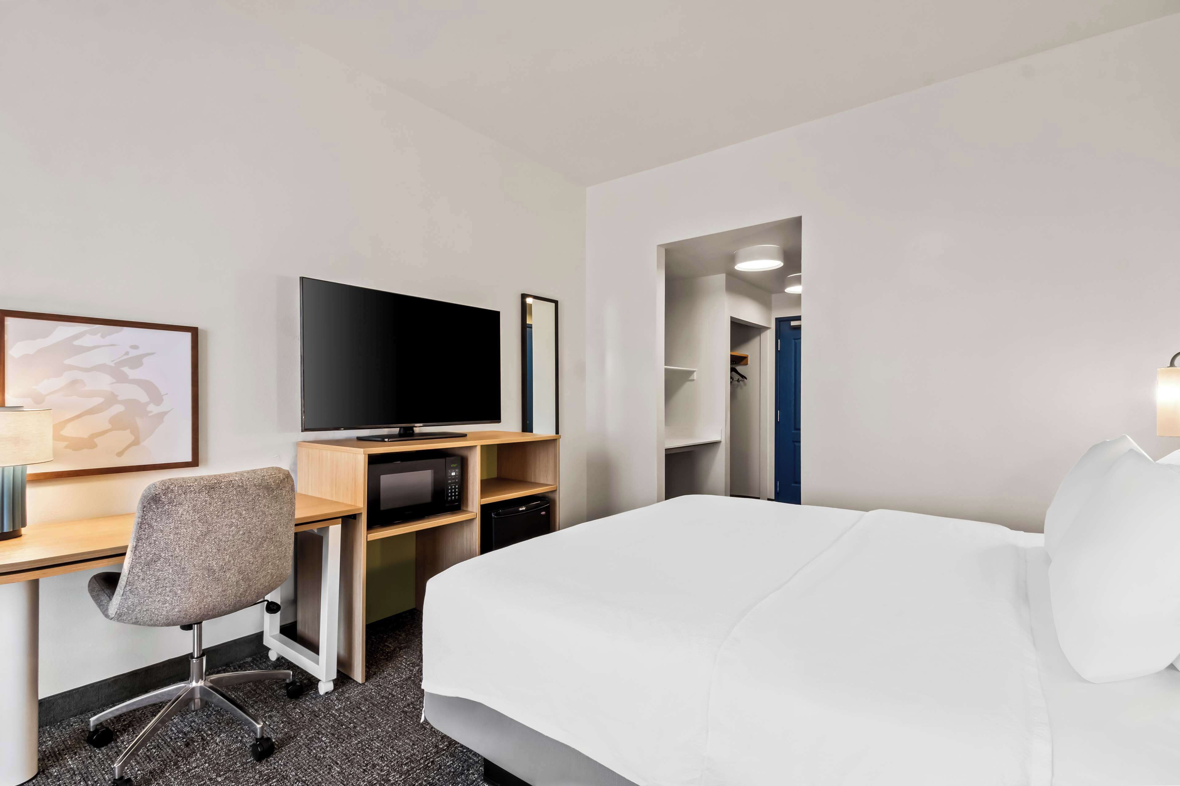 A hotel room with a bed, a desk with a computer, a television, and a microwave.